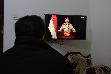 A person watches Houthi military spokesman Yahya Sarea as he delivers a televised statement