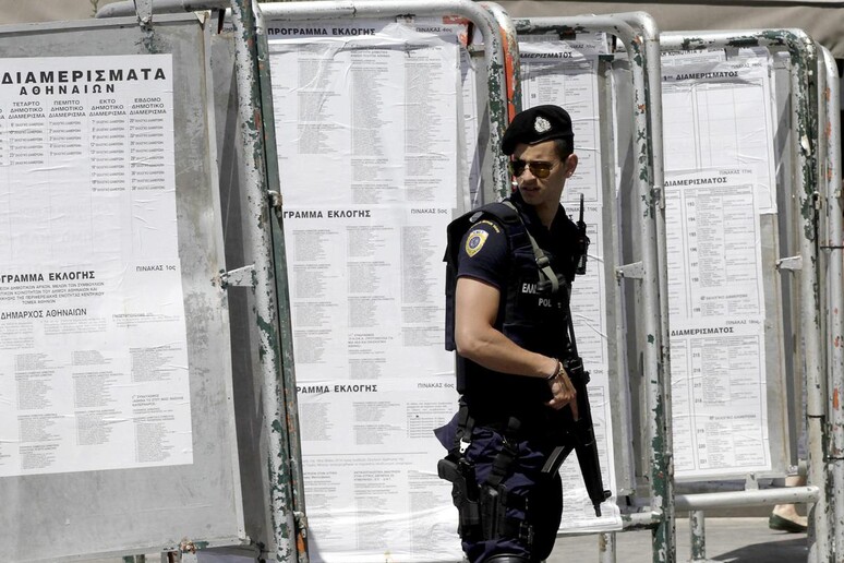 Un poliziotto davanti alle liste dei seggi elettorali per le Europee nel centro di Atene -     RIPRODUZIONE RISERVATA