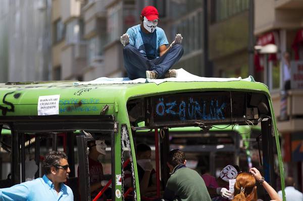 A protestor wearing a Guy Fawkes mask prays on top of a damaged public transport bus near Gezi Park in Taksim Square, Istanbul
