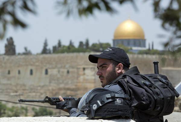 An Israeli riot policeman looks over as Palestinians prayed in the street of the neighborhood of Ras al-Amud