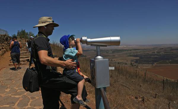 Israeli tourists watch the surrounding of the Israeli-Syrian border crossing Quneitra  from the Golan Heights,