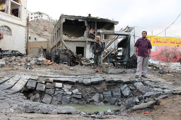 Men stand next to a crater made by a car bomb attack near the presidential palace in the southern port city of Aden, Yemen.