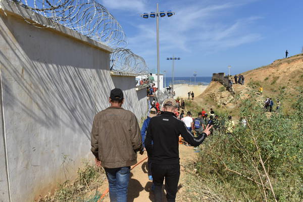 Migrants walk along a border wall in the northern town of Fnideq in an attempt to cross the border from Morocco to the Spanish enclave of Ceuta, in North Africa